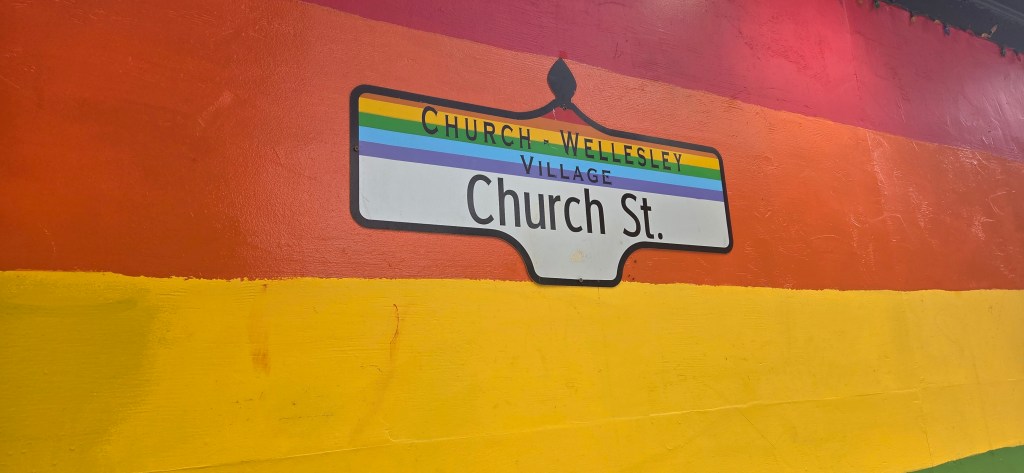 an image of the street sign of church Street in Toronto, with rainbow bands painted on the wall behind it